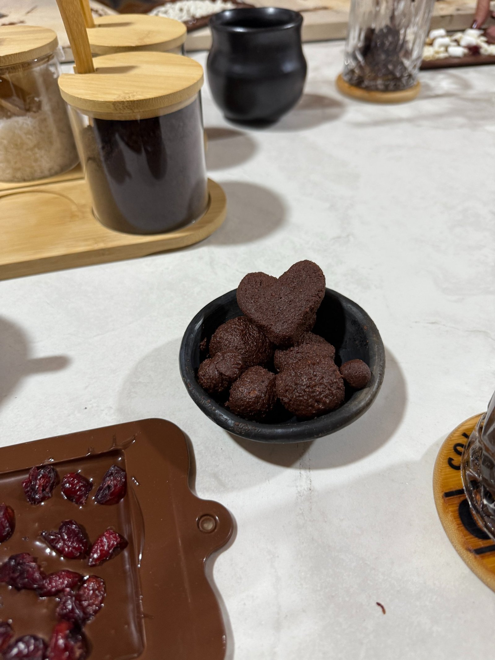 Heart-shaped dark chocolate truffles in a small black bowl on a white marble countertop.