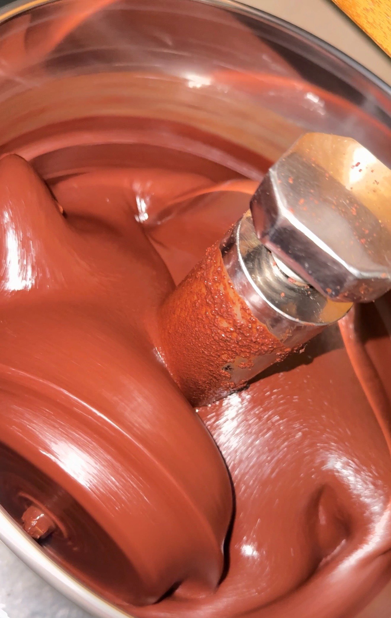 Smooth melted chocolate being mixed in a professional stone chocolate melanger machine.