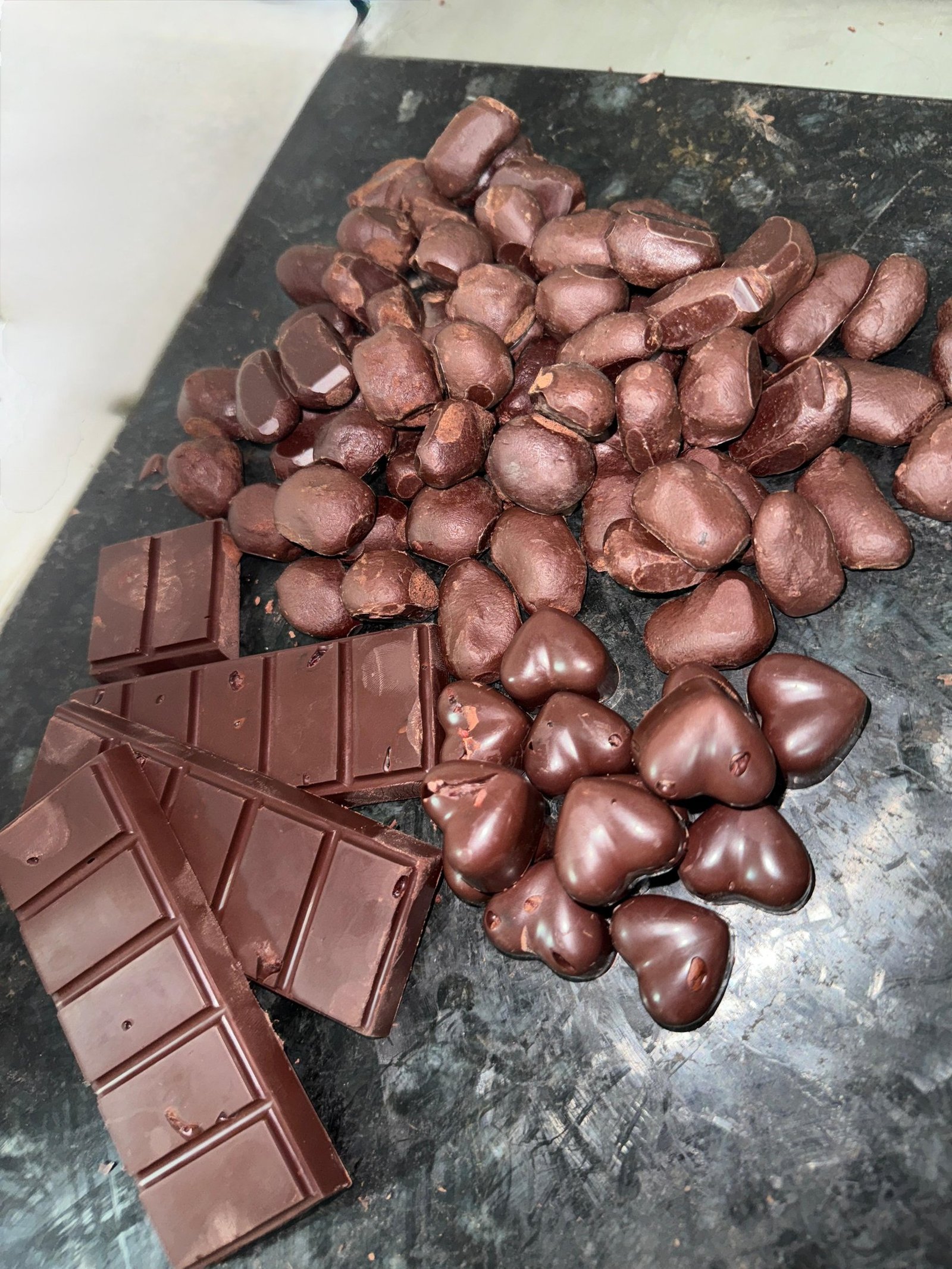 Dark chocolate bars and heart-shaped cocoa candies on a dark marble surface.