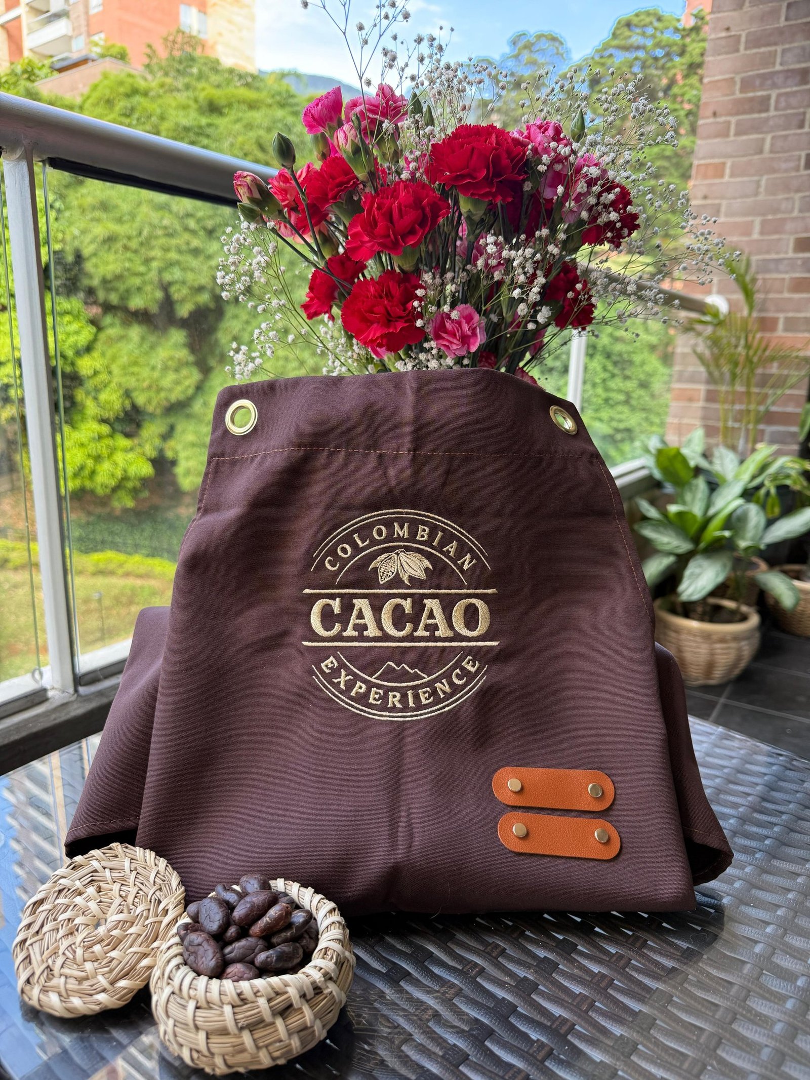 Brown Colombian Cacao Experience apron with red flowers and raw cocoa beans in a wicker basket.