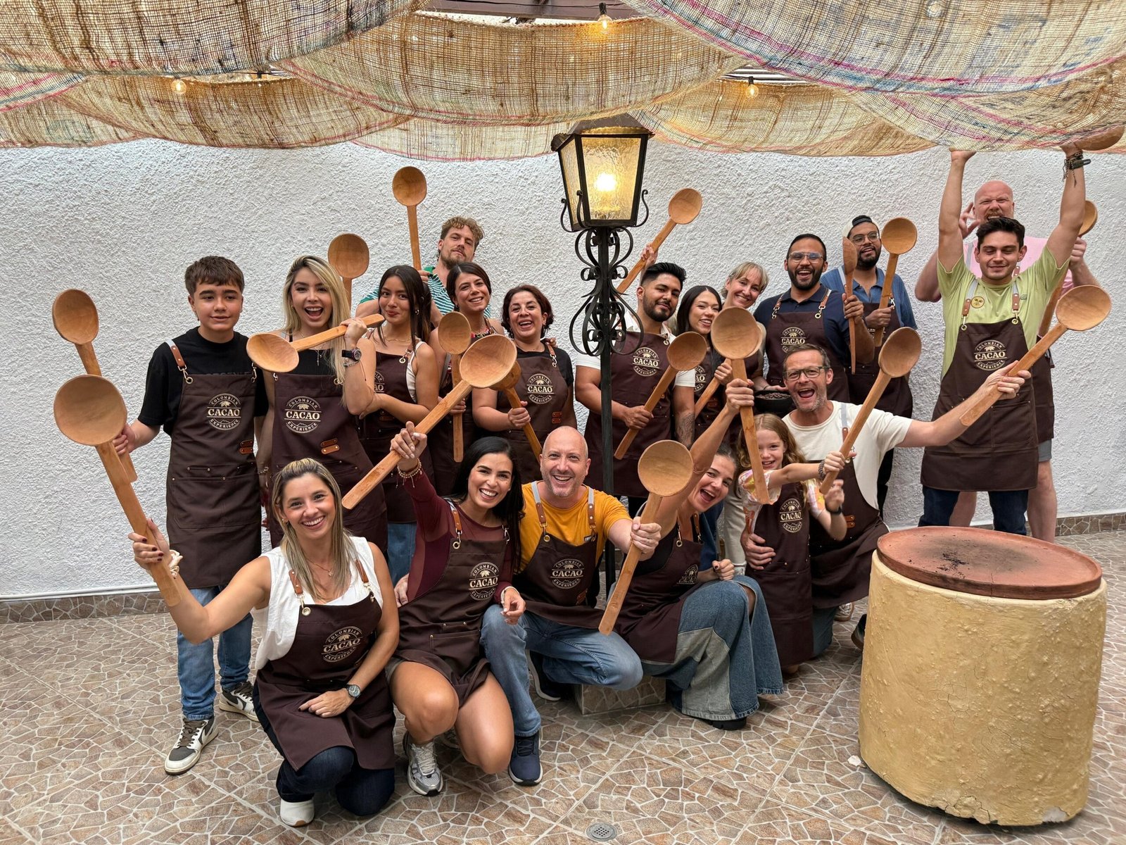 A group of diverse people in brown aprons holding large wooden spoons during a chocolate making workshop.